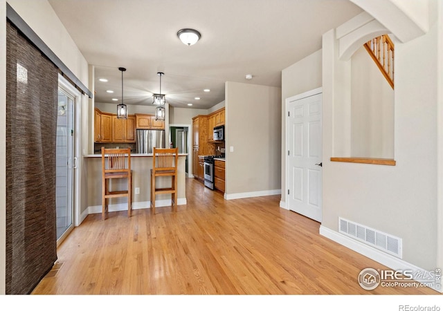 kitchen featuring appliances with stainless steel finishes, pendant lighting, a kitchen bar, and light hardwood / wood-style flooring