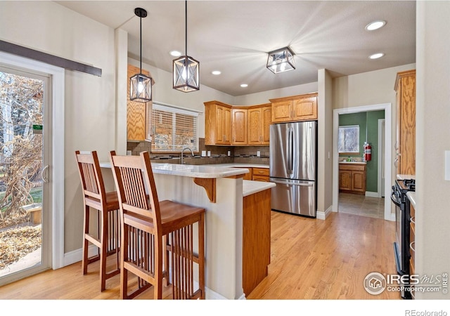 kitchen featuring a breakfast bar, range with gas stovetop, stainless steel refrigerator, hanging light fixtures, and kitchen peninsula