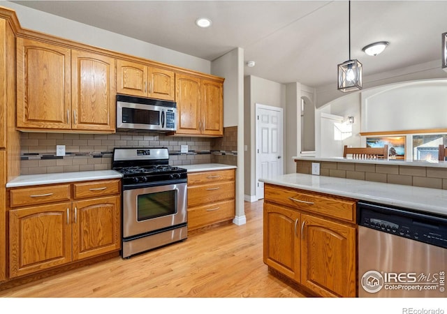 kitchen with appliances with stainless steel finishes, hanging light fixtures, decorative backsplash, and light wood-type flooring