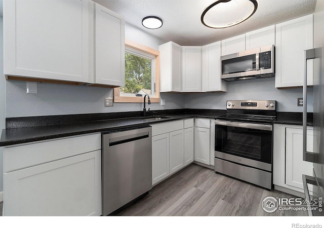 kitchen with white cabinets, stainless steel appliances, a textured ceiling, and light hardwood / wood-style floors