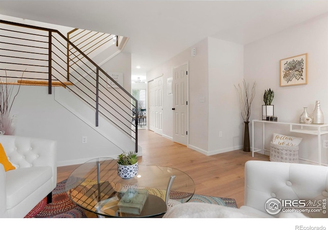 living area with light wood-type flooring, baseboards, and stairway