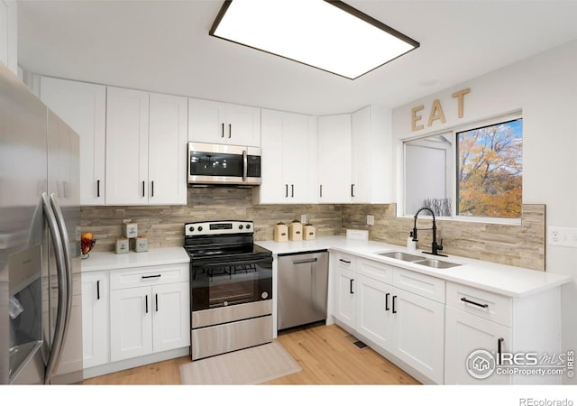 kitchen featuring appliances with stainless steel finishes, white cabinets, light countertops, and a sink