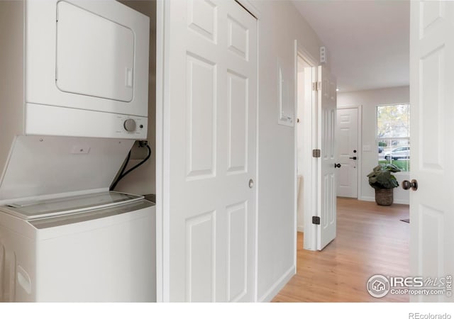 clothes washing area featuring laundry area, stacked washer and dryer, light wood-style flooring, and baseboards