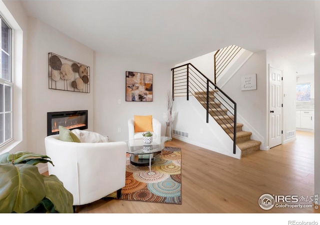 living room with visible vents, baseboards, light wood-style floors, stairway, and a glass covered fireplace