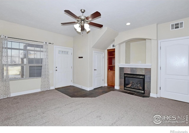 unfurnished living room featuring a tiled fireplace, ceiling fan, and dark carpet