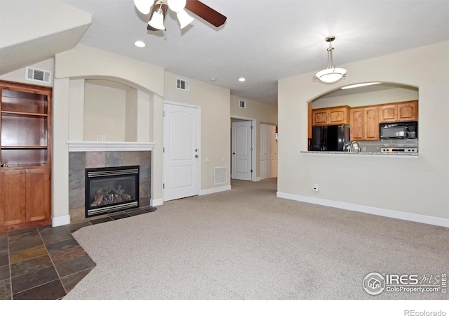 unfurnished living room with ceiling fan, a fireplace, and dark colored carpet