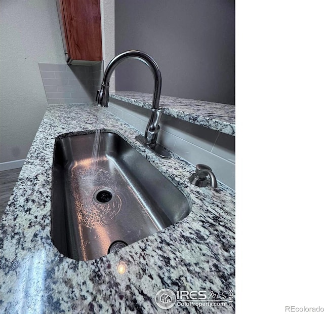 interior details featuring backsplash, light stone countertops, and sink