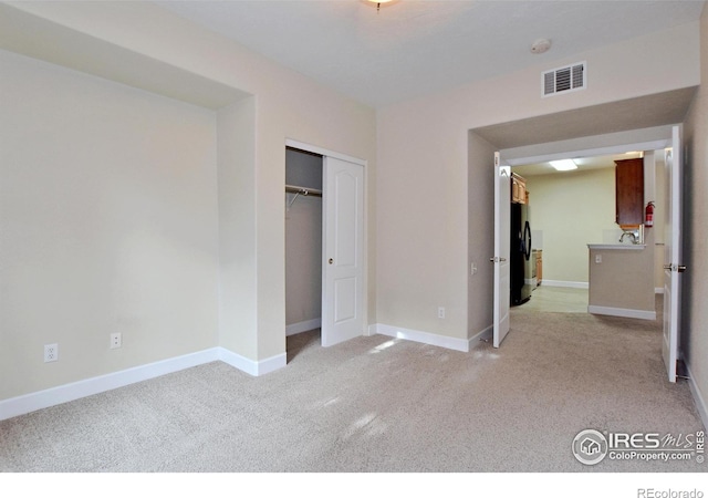 unfurnished bedroom featuring light carpet, a closet, and black refrigerator