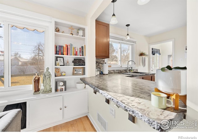 kitchen featuring backsplash, sink, decorative light fixtures, and light wood-type flooring