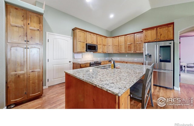 kitchen with light stone countertops, stainless steel appliances, sink, lofted ceiling, and an island with sink