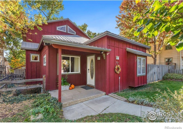 chalet / cabin with a standing seam roof, metal roof, board and batten siding, and fence