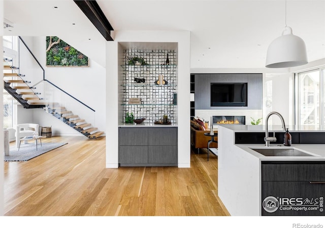 kitchen with beamed ceiling, light wood-type flooring, decorative light fixtures, and sink