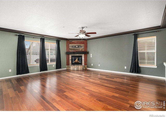 unfurnished living room featuring hardwood / wood-style flooring, ceiling fan, a large fireplace, and crown molding