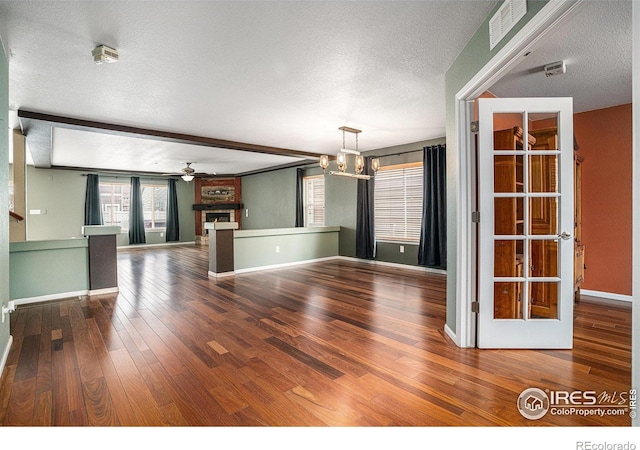 unfurnished living room featuring a textured ceiling, a large fireplace, ceiling fan with notable chandelier, beamed ceiling, and hardwood / wood-style floors