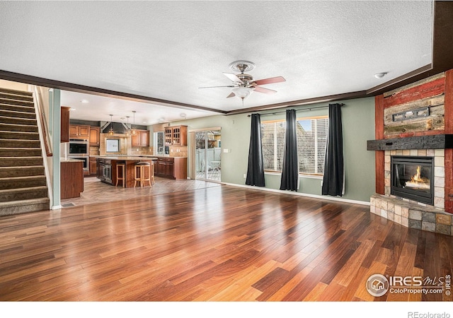 living room featuring hardwood / wood-style floors, a textured ceiling, a stone fireplace, and ceiling fan