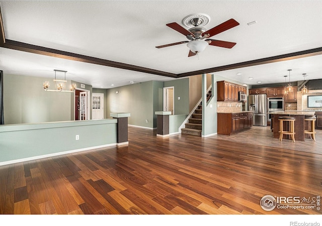 unfurnished living room featuring beamed ceiling, ceiling fan with notable chandelier, dark hardwood / wood-style flooring, and a textured ceiling