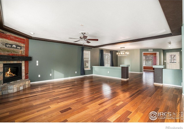 unfurnished living room with a stone fireplace, crown molding, wood-type flooring, and ceiling fan with notable chandelier