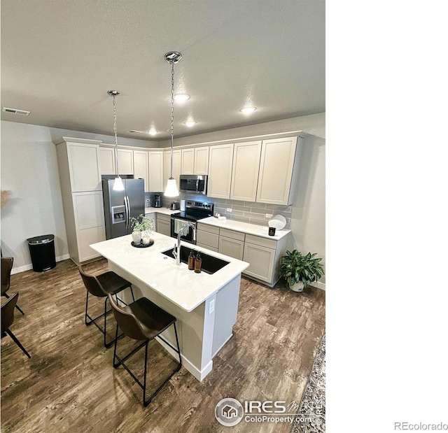 kitchen featuring decorative backsplash, appliances with stainless steel finishes, sink, pendant lighting, and a center island with sink