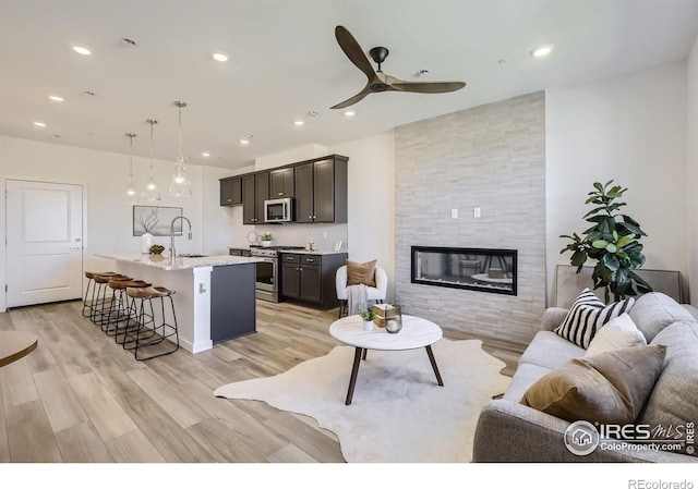 living room featuring sink, ceiling fan, light hardwood / wood-style floors, and a tiled fireplace