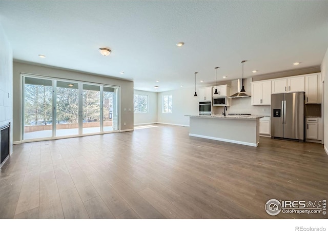 kitchen with pendant lighting, appliances with stainless steel finishes, light stone counters, white cabinets, and wall chimney exhaust hood