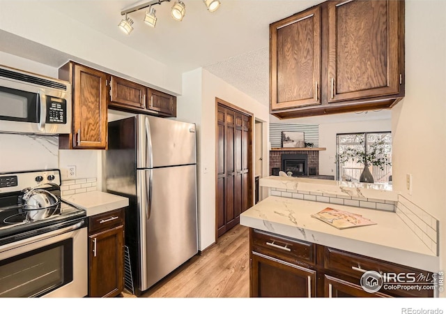 kitchen featuring light hardwood / wood-style flooring, a textured ceiling, a fireplace, dark brown cabinets, and stainless steel appliances