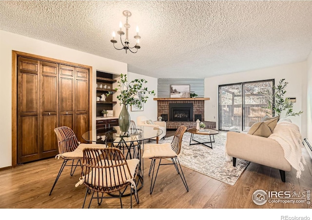 dining area with a textured ceiling, a notable chandelier, a fireplace, and hardwood / wood-style flooring