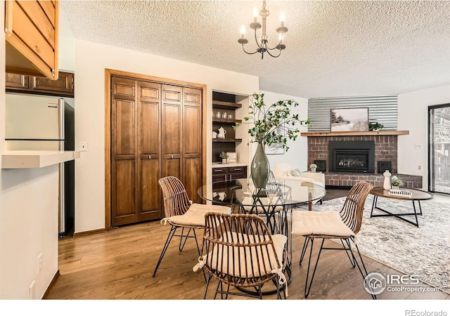 dining area with a fireplace, a textured ceiling, light wood-type flooring, and an inviting chandelier