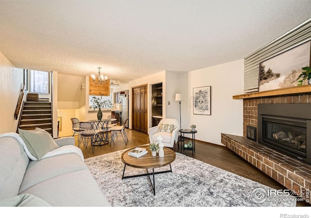 living room with dark hardwood / wood-style flooring, an inviting chandelier, a textured ceiling, and a brick fireplace