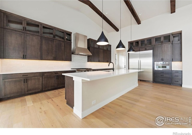 kitchen featuring appliances with stainless steel finishes, wall chimney exhaust hood, sink, decorative light fixtures, and beam ceiling