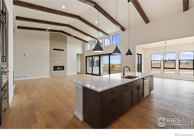 kitchen with decorative light fixtures, beamed ceiling, a fireplace, sink, and a kitchen island with sink