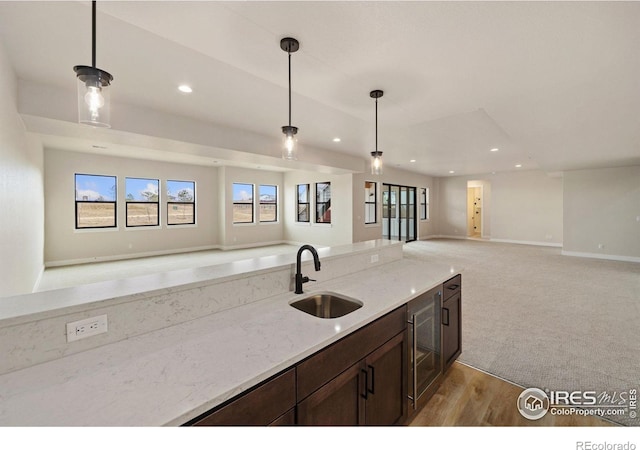 kitchen featuring sink, beverage cooler, hanging light fixtures, and light stone counters