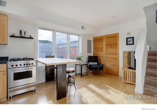 kitchen with high end range, light brown cabinets, electric panel, and light hardwood / wood-style flooring