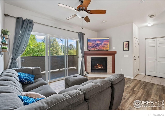 living room with a tile fireplace, wood-type flooring, and ceiling fan