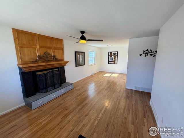 unfurnished living room with visible vents, a tiled fireplace, a ceiling fan, wood finished floors, and baseboards