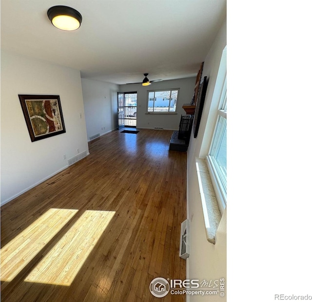 unfurnished living room featuring a ceiling fan, a fireplace with raised hearth, and hardwood / wood-style flooring