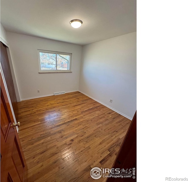 unfurnished bedroom featuring wood-type flooring, a closet, visible vents, and baseboards