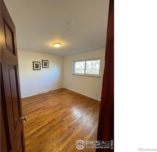 spare room with baseboards, visible vents, and hardwood / wood-style floors