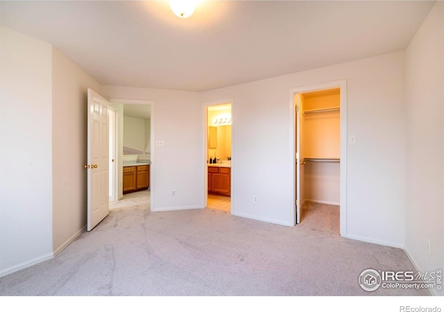 unfurnished bedroom featuring connected bathroom, a walk in closet, a closet, and light colored carpet