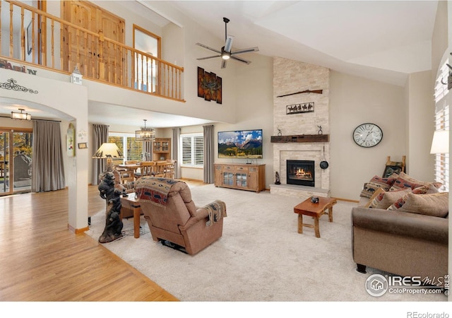 living room with a stone fireplace, hardwood / wood-style floors, high vaulted ceiling, and ceiling fan with notable chandelier