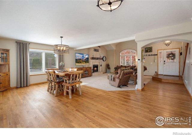 dining space featuring a fireplace, light hardwood / wood-style flooring, vaulted ceiling, and a chandelier