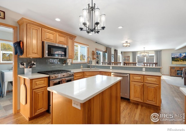 kitchen with kitchen peninsula, appliances with stainless steel finishes, sink, pendant lighting, and a kitchen island