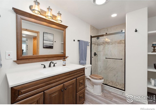 bathroom with hardwood / wood-style floors, vanity, toilet, and a shower with shower door