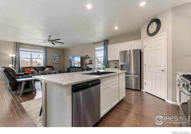 kitchen with sink, a kitchen island with sink, stainless steel appliances, white cabinets, and dark hardwood / wood-style flooring