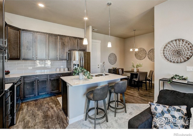 kitchen featuring decorative light fixtures, tasteful backsplash, a kitchen island with sink, stainless steel appliances, and dark brown cabinets