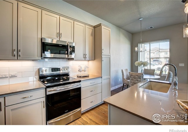 kitchen featuring appliances with stainless steel finishes, light wood-type flooring, hanging light fixtures, and sink