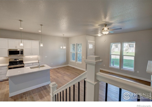 kitchen with ceiling fan with notable chandelier, stainless steel appliances, sink, pendant lighting, and white cabinets