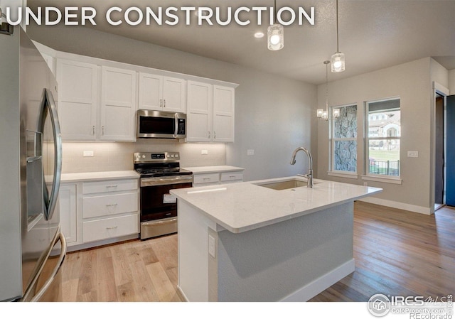 kitchen with white cabinetry, hanging light fixtures, a kitchen island with sink, appliances with stainless steel finishes, and light wood-type flooring