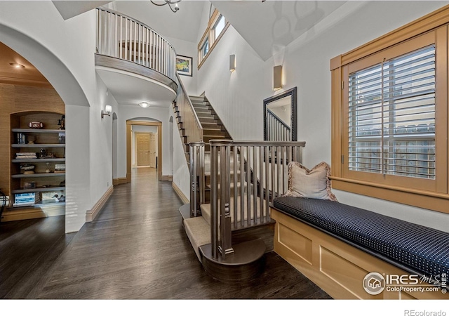 hallway with built in shelves, dark wood-type flooring, and a high ceiling