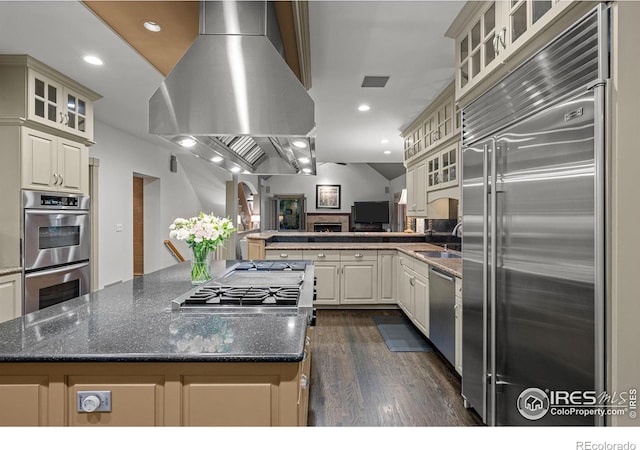 kitchen with dark stone counters, island range hood, a center island, and stainless steel appliances