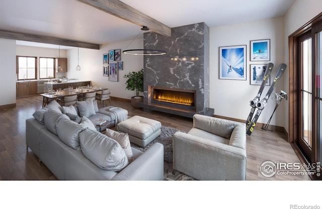 living room featuring beam ceiling, hardwood / wood-style floors, a high end fireplace, and a chandelier